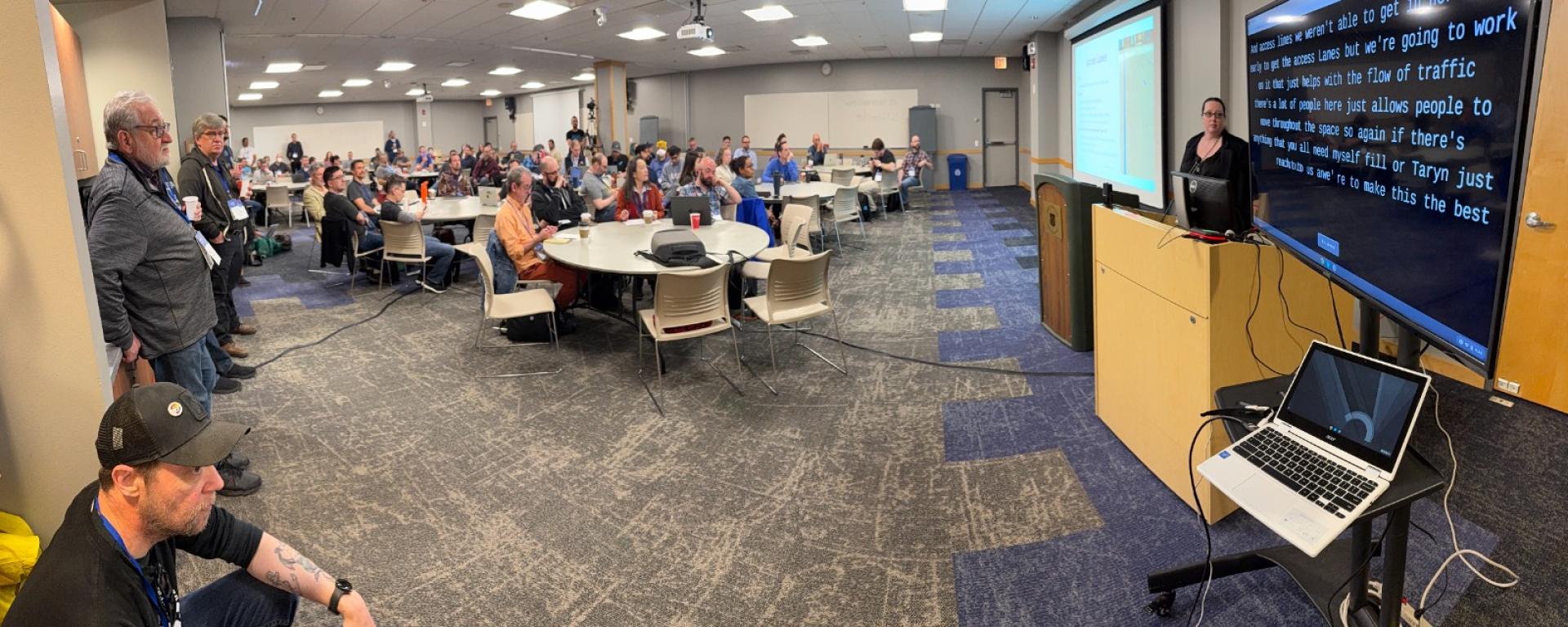 Norah Shannon Medlin welcomes the delegates at Midwest Drupal Camp (MidCamp) 2025. Live caption can be seen in the screen to her left. Norah Shannon Medlin welcomes the delegates at Midwest Drupal Camp (MidCamp) 2025. Live caption can be seen in the screen to her left.