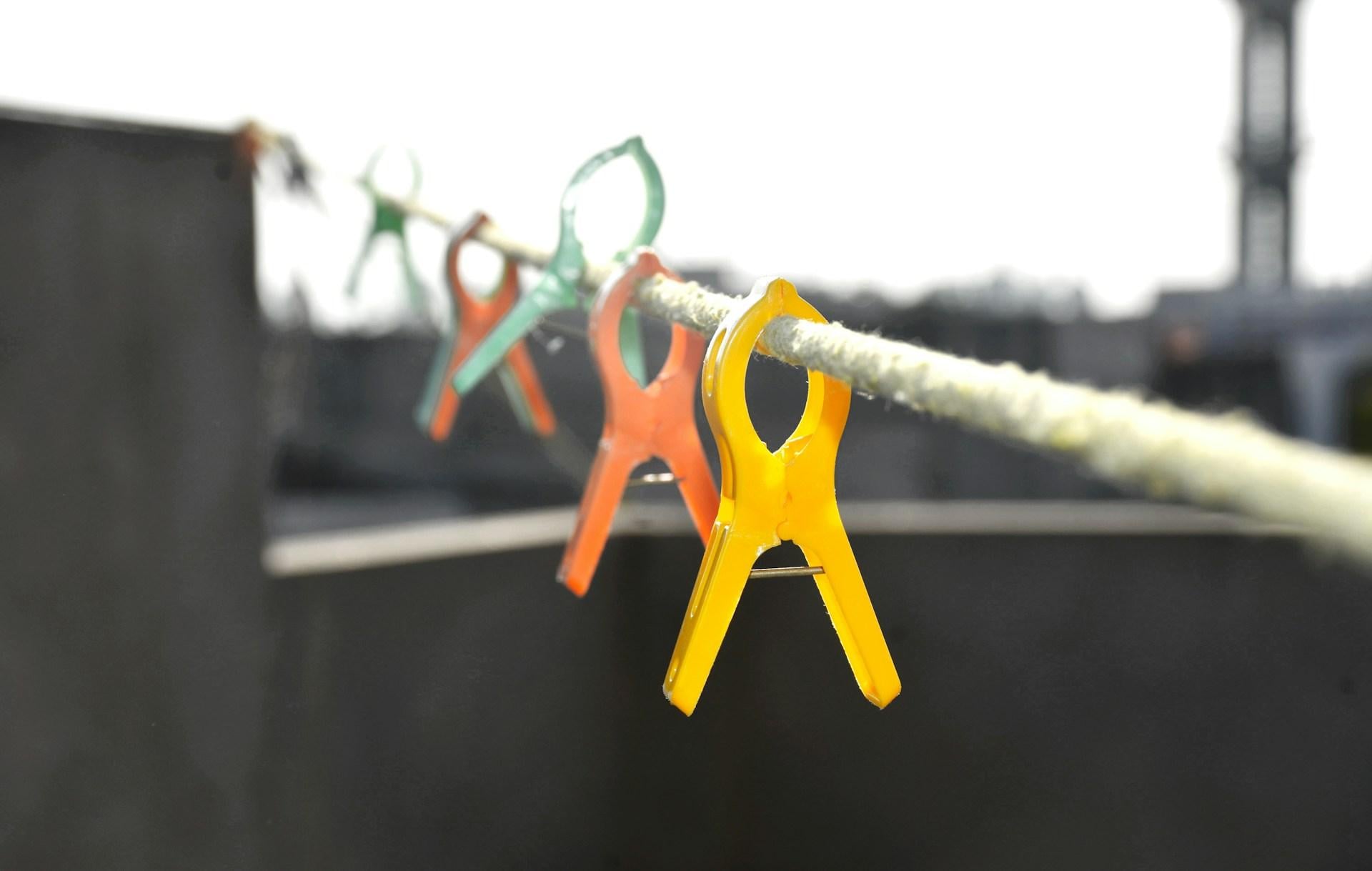 Bright yellow, orange, and green clothespins clipped along a rope against a dark background, demonstrating strong colour contrast.