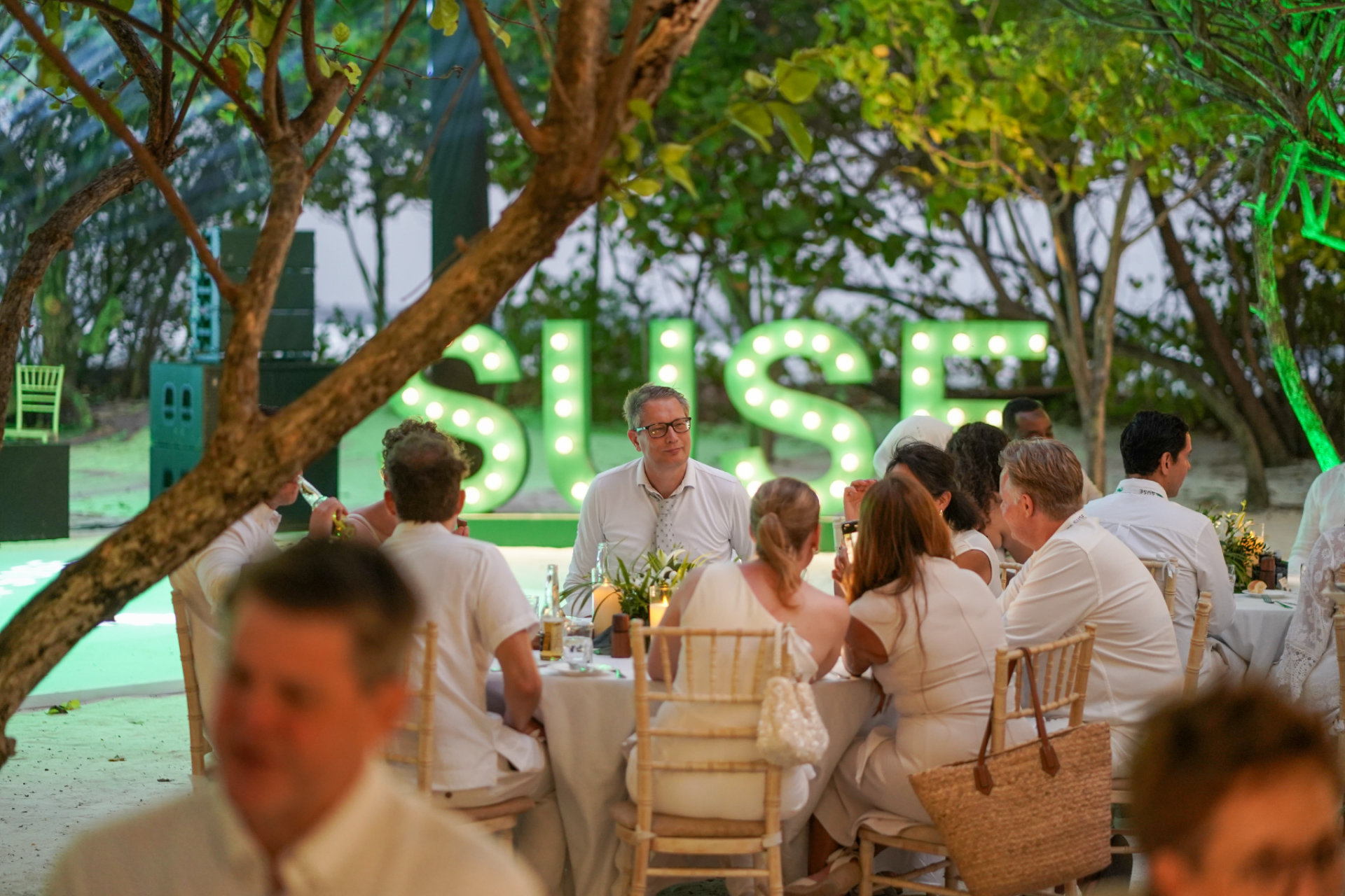 Bert Boerland seated at an evening event table, with other attendees and illuminated event lettering in the background.