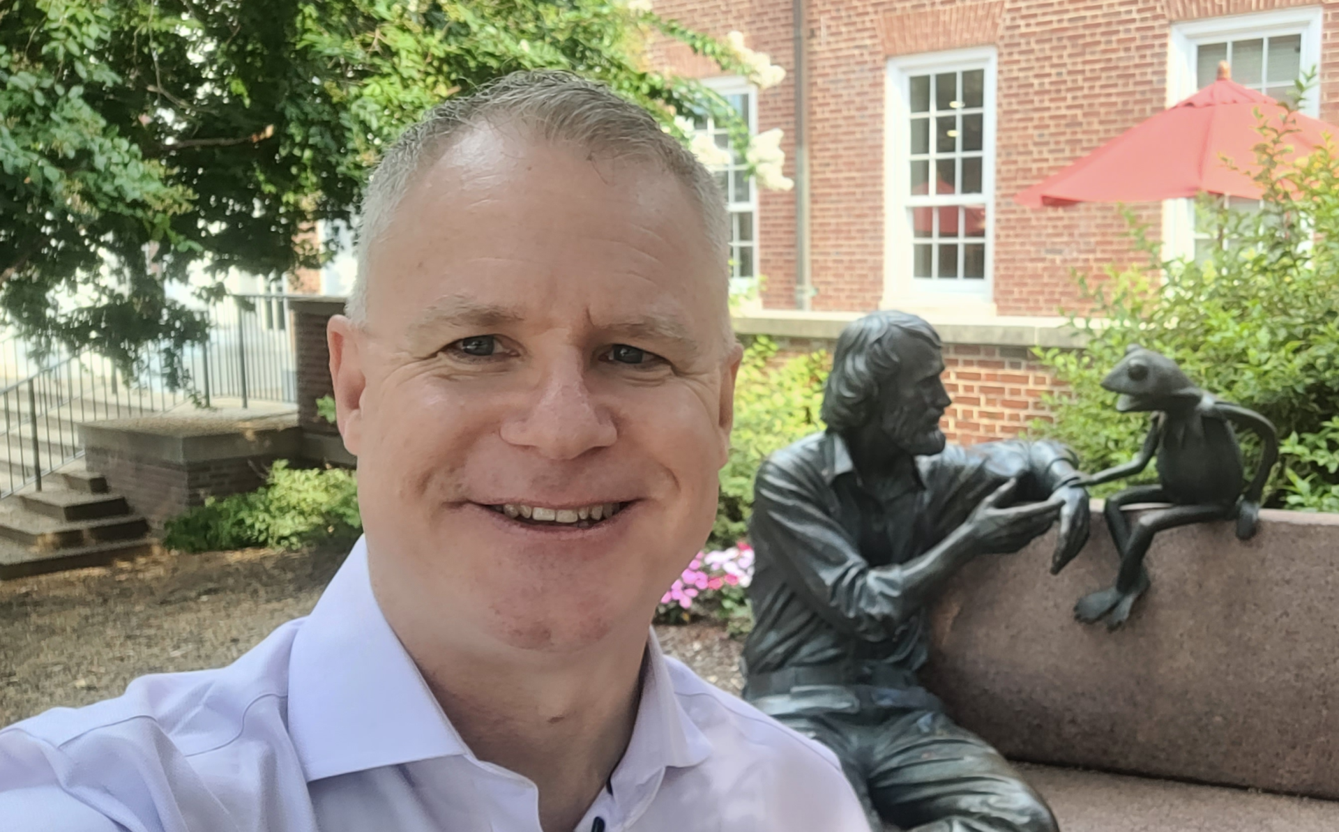 Chad Capellman taking a selfie outdoors on the University of Maryland campus, with the Jim Henson and Kermit the Frog bench statue behind him.