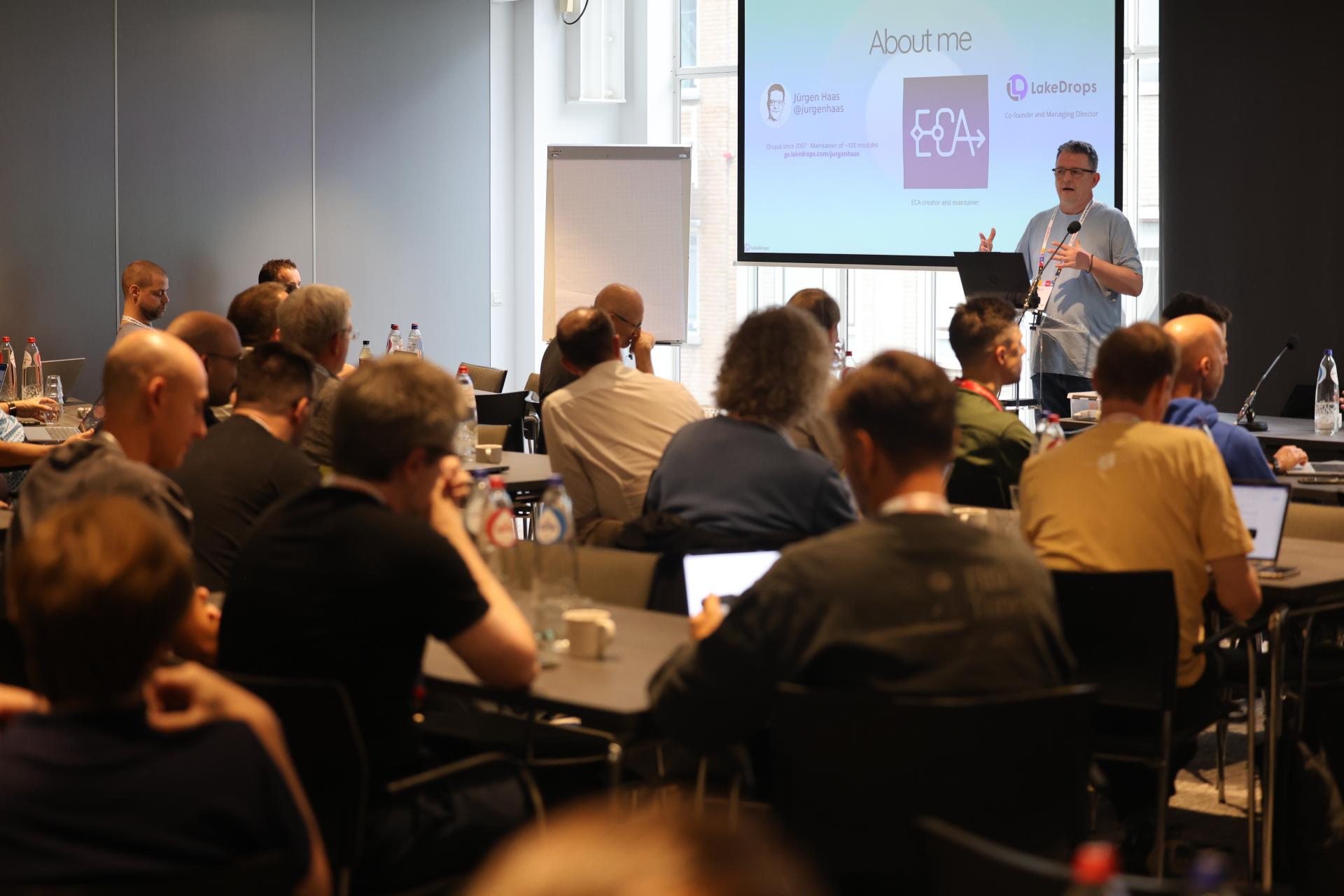 Jürgen Haas presenting an ECA slide to attendees seated in a conference room at the AI Dev Summit in Rotterdam.