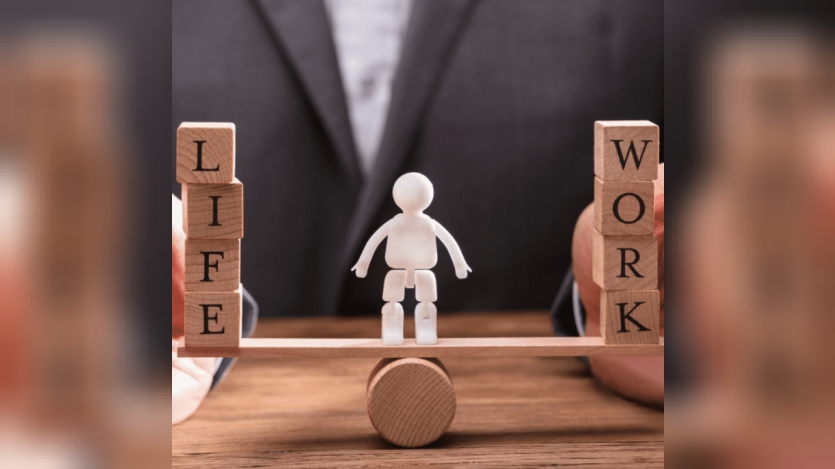 Demonstrating Work Life Balance using a tiny wooden seesaw with wooden blocks on either side and a small white human effigy on the center