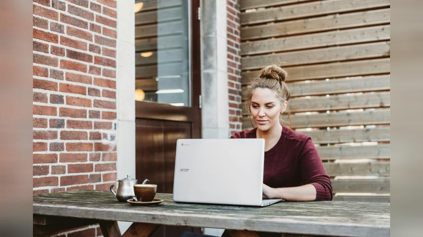 oman-sitting-and-holding-white-acer-laptop-near-brown-wooden-wall