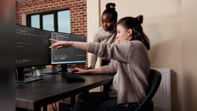 Caucasian network developer pointing out high usage of processing power in mainframe grid. African american programmer helping coworker to solve overloaded system storage space.