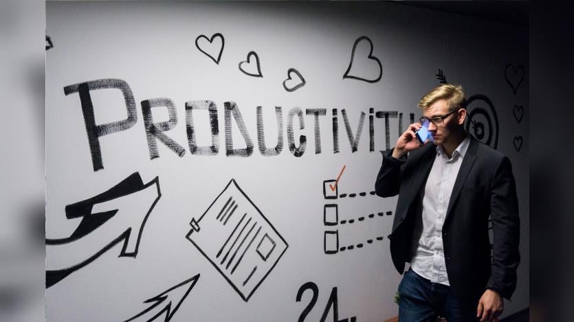 A man talking over the mobile phone passing by a wall with graffity that says about productivity