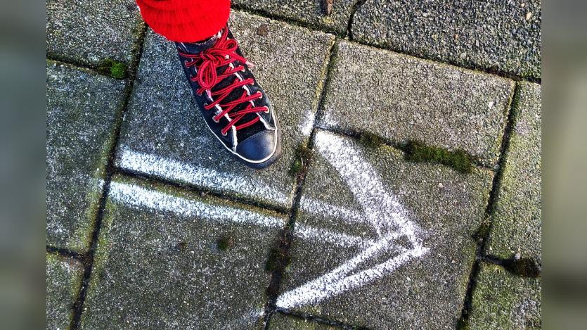 A person's foot wearing a shoe and a an arrow drawn on the pavement