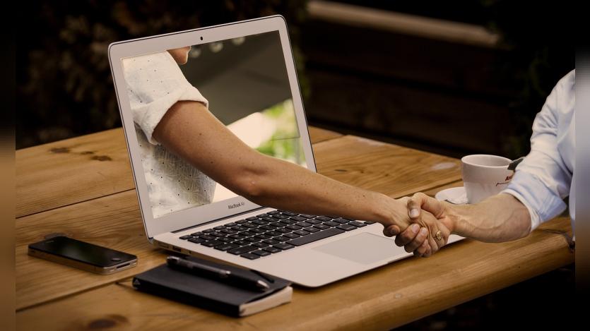 a man shaking hands with a hand projecting out of a laptop screen