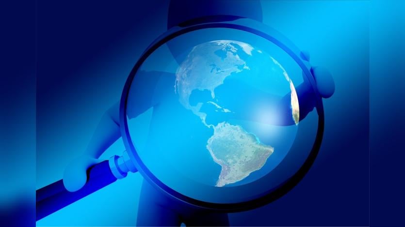 A giant magnifying lens held in the hands of a human figure, with the image of earth in the middle