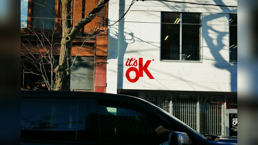 A van is parked outside of a building. 'It's Ok!' is written on the wall of the building.