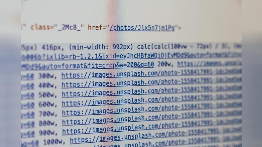 Close-up photograph of HTML and image URL code displayed on a computer screen, showing multiple links to images hosted on Unsplash. The code includes attributes such as width settings, formatting parameters, and image source URLs, with parts of the text slightly blurred.