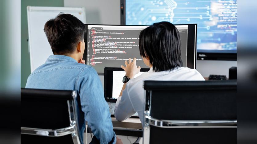 Two developers working together in an office, discussing code on a screen