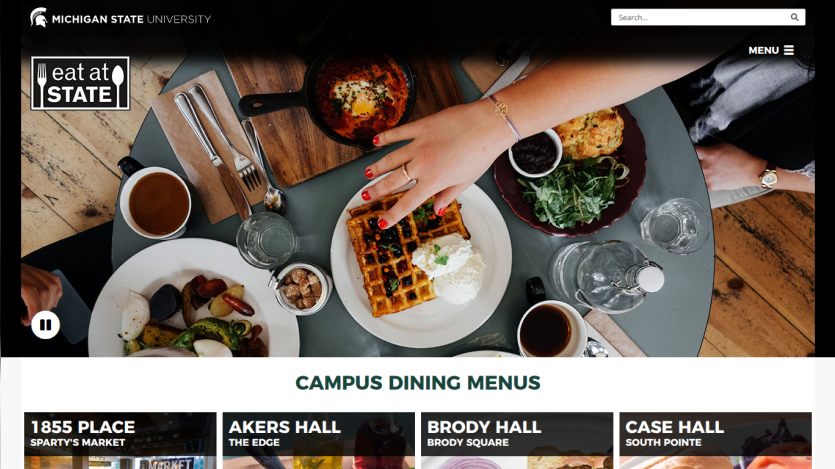 A dining table with various dishes and drinks, featuring a hand reaching for a waffle.