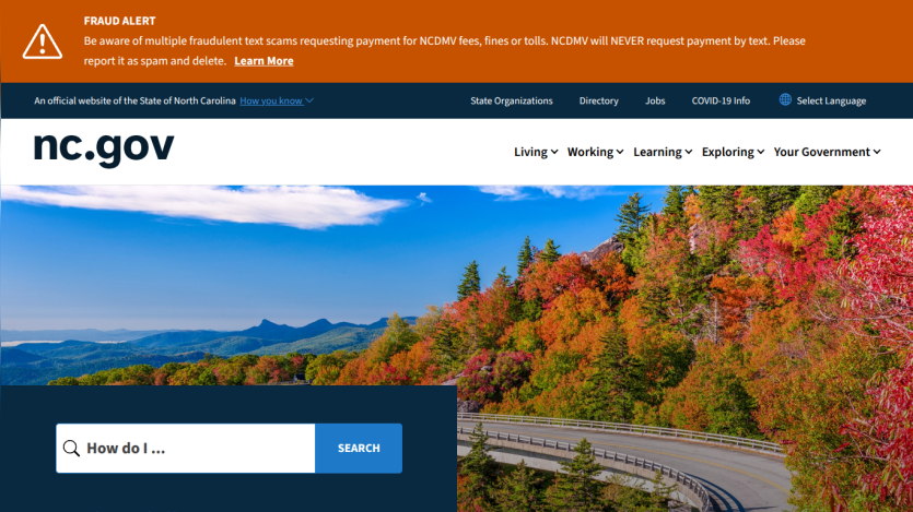 North Carolina government website with navigation menu, fraud alert banner, and search bar over scenic mountain road in autumn