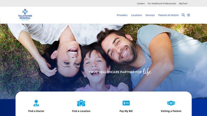 Healthcare website homepage with smiling family on grass, navigation menu, and options to find a doctor, location, pay bill, and visit patient
