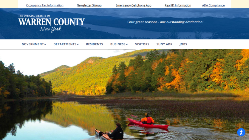 Official website of Warren County New York with navigation links and a hero image of two kayakers on a lake surrounded by autumn trees