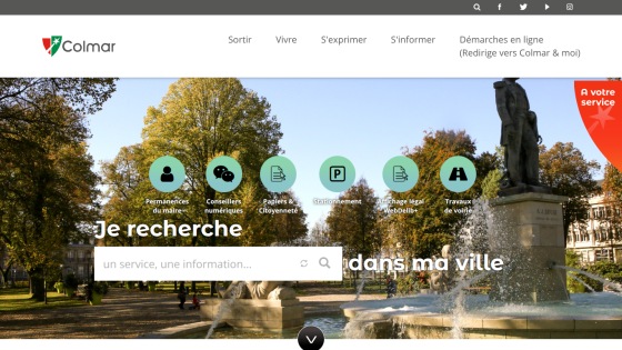 City of Colmar website with navigation menu, search bar, and icons for mayor's office, digital advisors, citizenship papers, parking, legal notices, and roadworks over a park fountain background