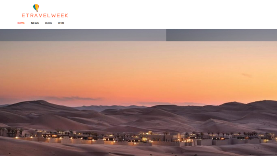 Etravelweek website featuring a sunset view over desert dunes and illuminated buildings.