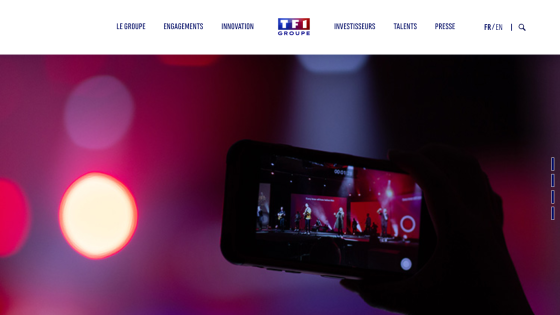 Website header with navigation links and a hero section showing a hand holding a phone capturing a stage performance with red lighting