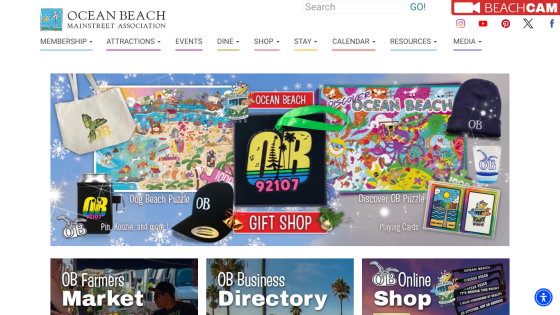 Ocean Beach Mainstreet Association website with navigation menu and gift shop promotion featuring puzzles, apparel, and accessories