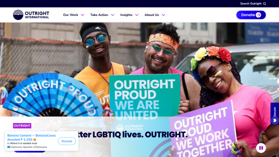 Three individuals celebrating with signs promoting LGBTQ+ pride and unity.