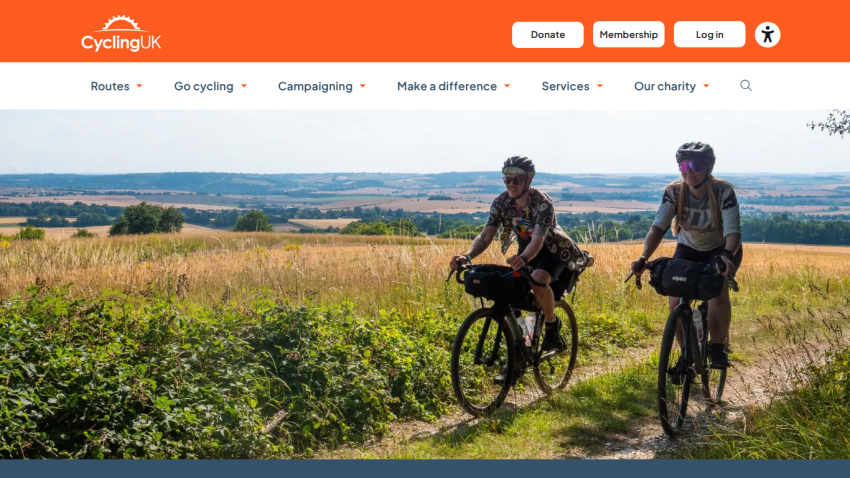 Two cyclists riding on a scenic trail with fields in the background.