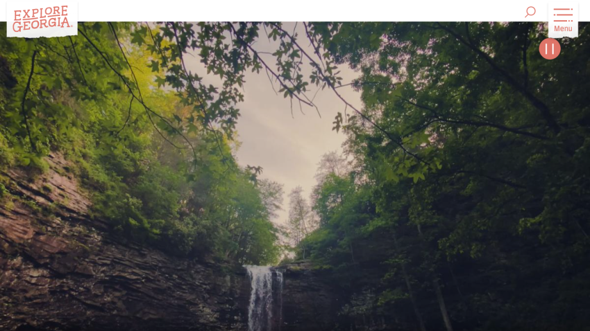 A scenic view of a waterfall surrounded by lush greenery, with a logo at the top.