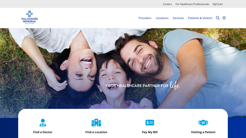 Healthcare website homepage with smiling family on grass, navigation menu, and options to find a doctor, location, pay bill, and visit patient