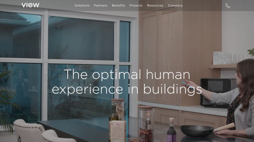 Website header with navigation and hero section showing two people talking by a window overlooking a lake, text 'The optimal human experience in buildings'