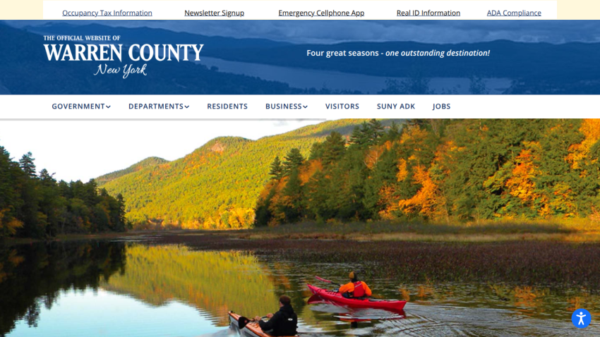 Official website of Warren County New York with navigation links and a hero image of two kayakers on a lake surrounded by autumn trees