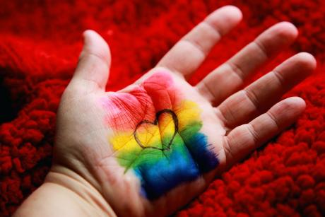 Photo captured by Alexander Grey taken from unsplash.com. The picture shows a hand with diversity flag colours painted on the palm and a heart in black ink over it.