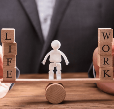 Demonstrating Work Life Balance using a tiny wooden seesaw with wooden blocks on either side and a small white human effigy on the center