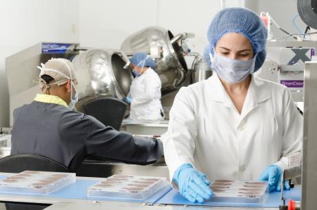 Three people inside a factory wearing masks and coats