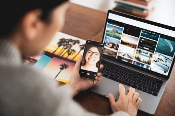 A man video calling his wife on phone infront of a laptop