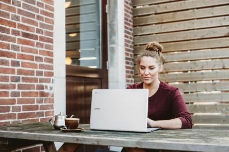 oman-sitting-and-holding-white-acer-laptop-near-brown-wooden-wall