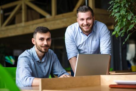 Picture of handsome businessman listening to his colleague or partner concerning ner business system while working on laptop computer in office interior