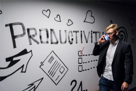 A man talking over the mobile phone passing by a wall with graffity that says about productivity