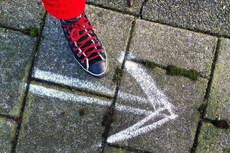 A person's foot wearing a shoe and a an arrow drawn on the pavement