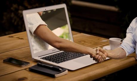 a man shaking hands with a hand projecting out of a laptop screen