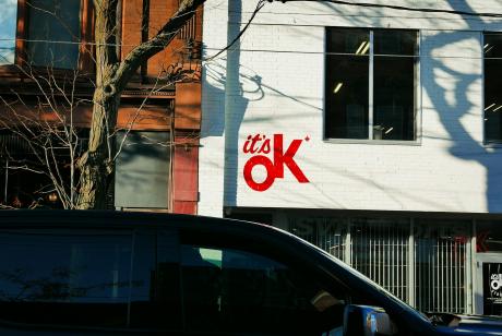 A van is parked outside of a building. 'It's Ok!' is written on the wall of the building.