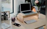 A workdesk with a laptop, wireless keyboard, mobile phone, a book, teacup, pencil holder, flowervase and other things near a glass window