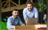 Picture of handsome businessman listening to his colleague or partner concerning ner business system while working on laptop computer in office interior