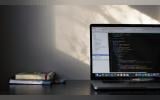 Light falling on a desk from an unseen window, a laptop with code and two books are placed on the table.