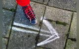 A person's foot wearing a shoe and a an arrow drawn on the pavement