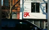 A van is parked outside of a building. 'It's Ok!' is written on the wall of the building.